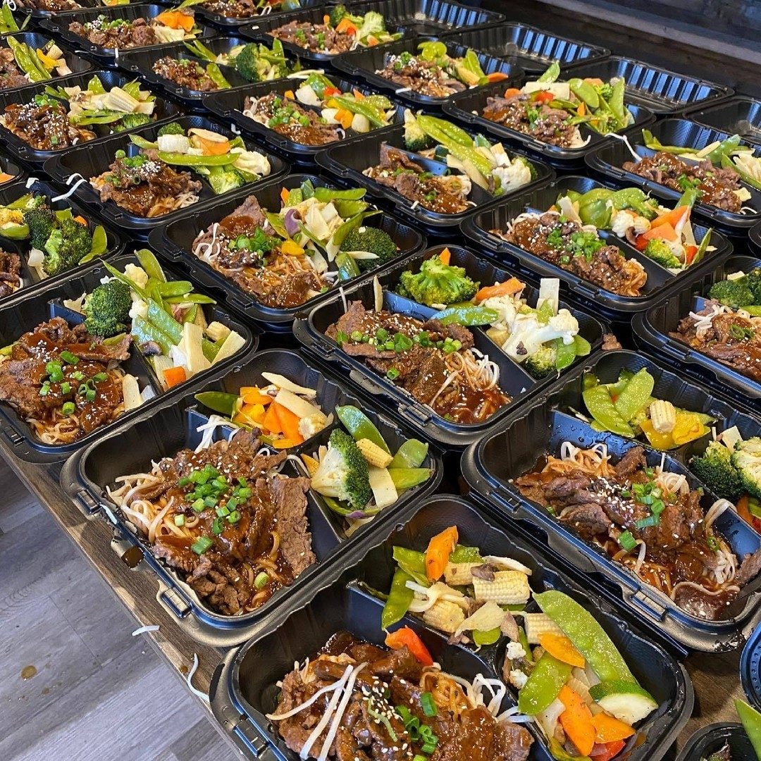 Rows of boxed lunches with glazed beef, noodles and stir-fried vegetables
