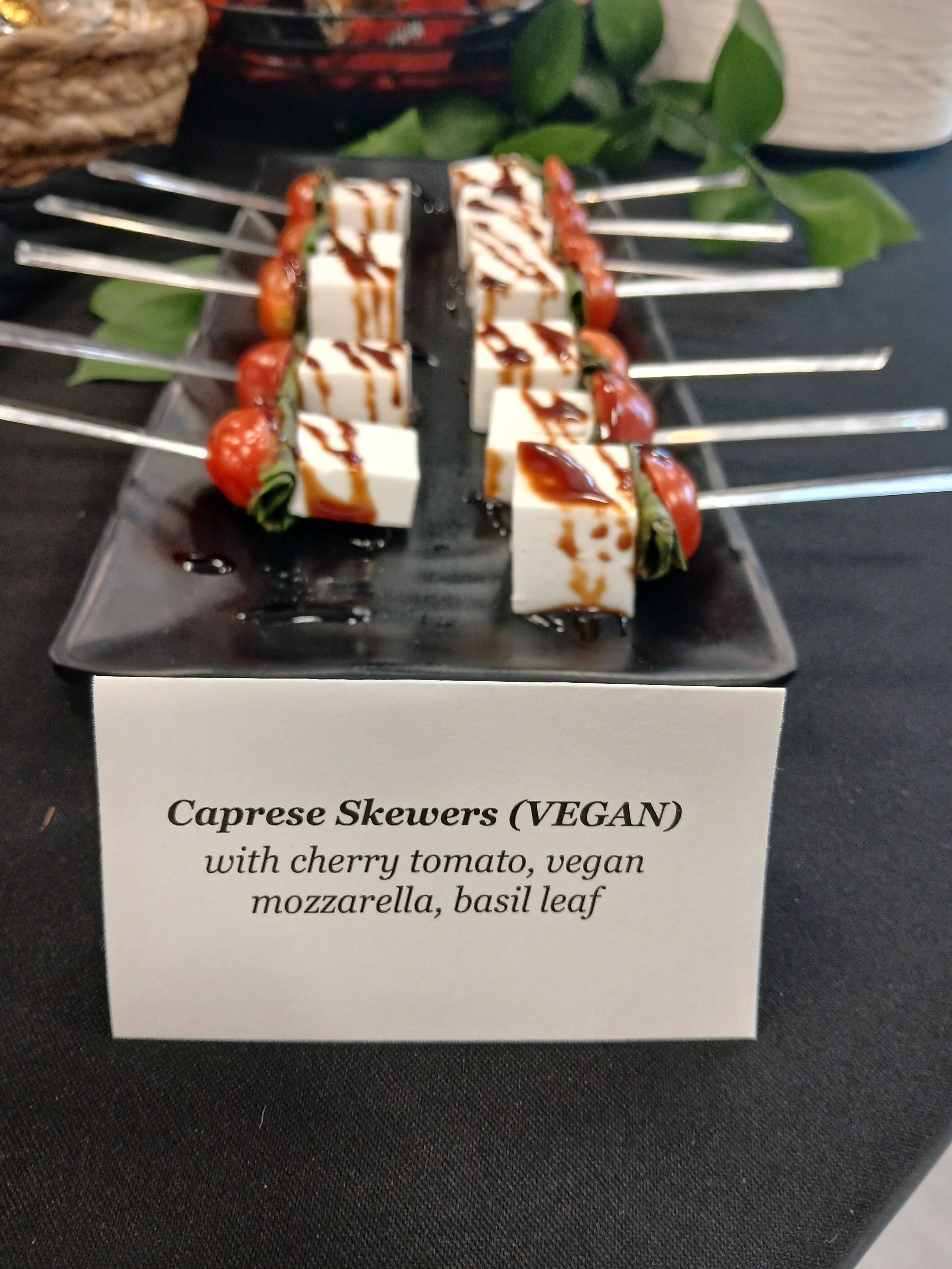 Vegan caprese skewers with cherry tomato, vegan mozzarella, and basil leaf drizzled with balsamic glaze on a black plate — Atlanta corporate event catering