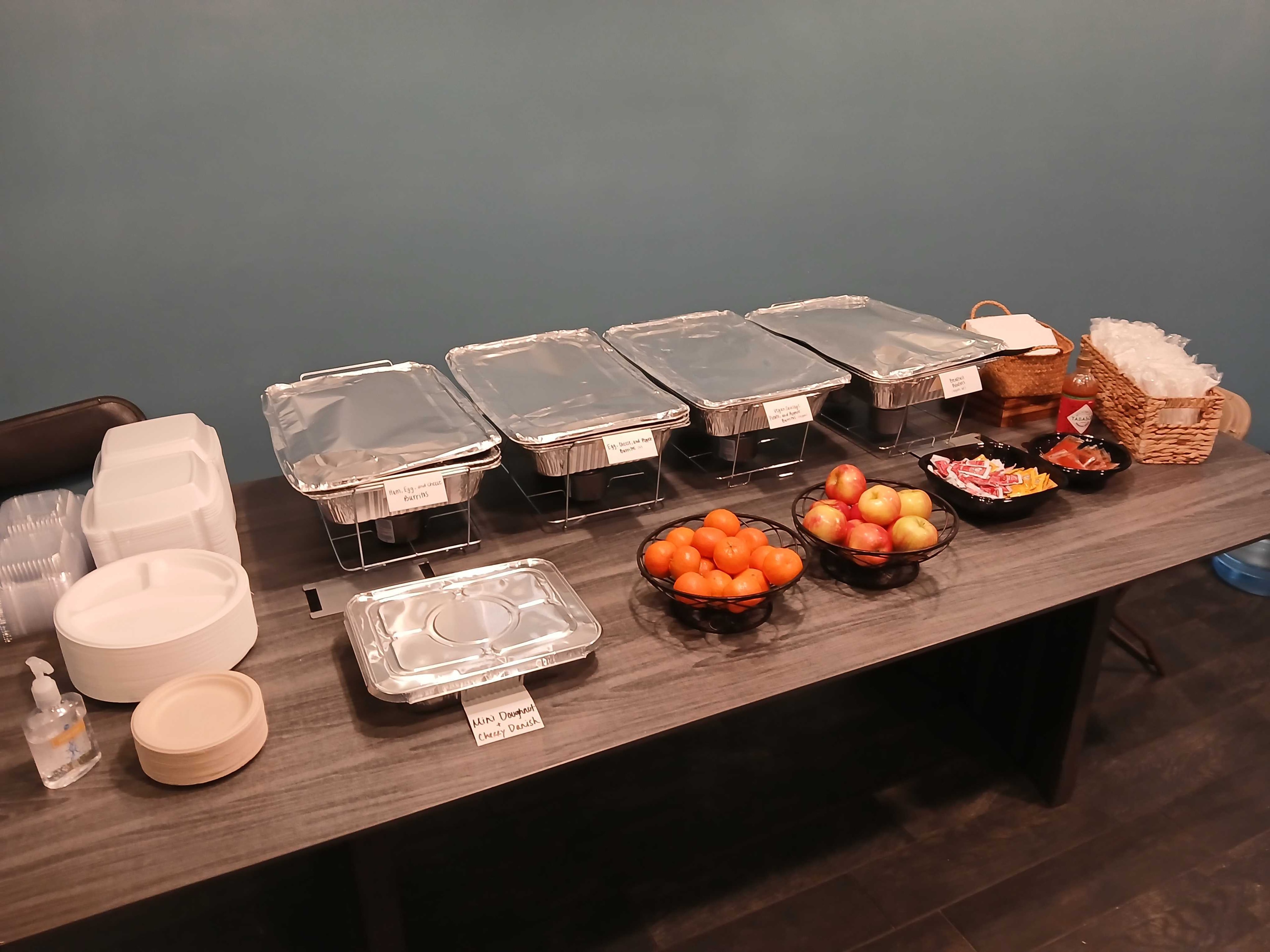 Atlanta production catering breakfast setup — chafing dishes with egg muffins, mini donuts, fresh fruit, and labeled menu cards on set