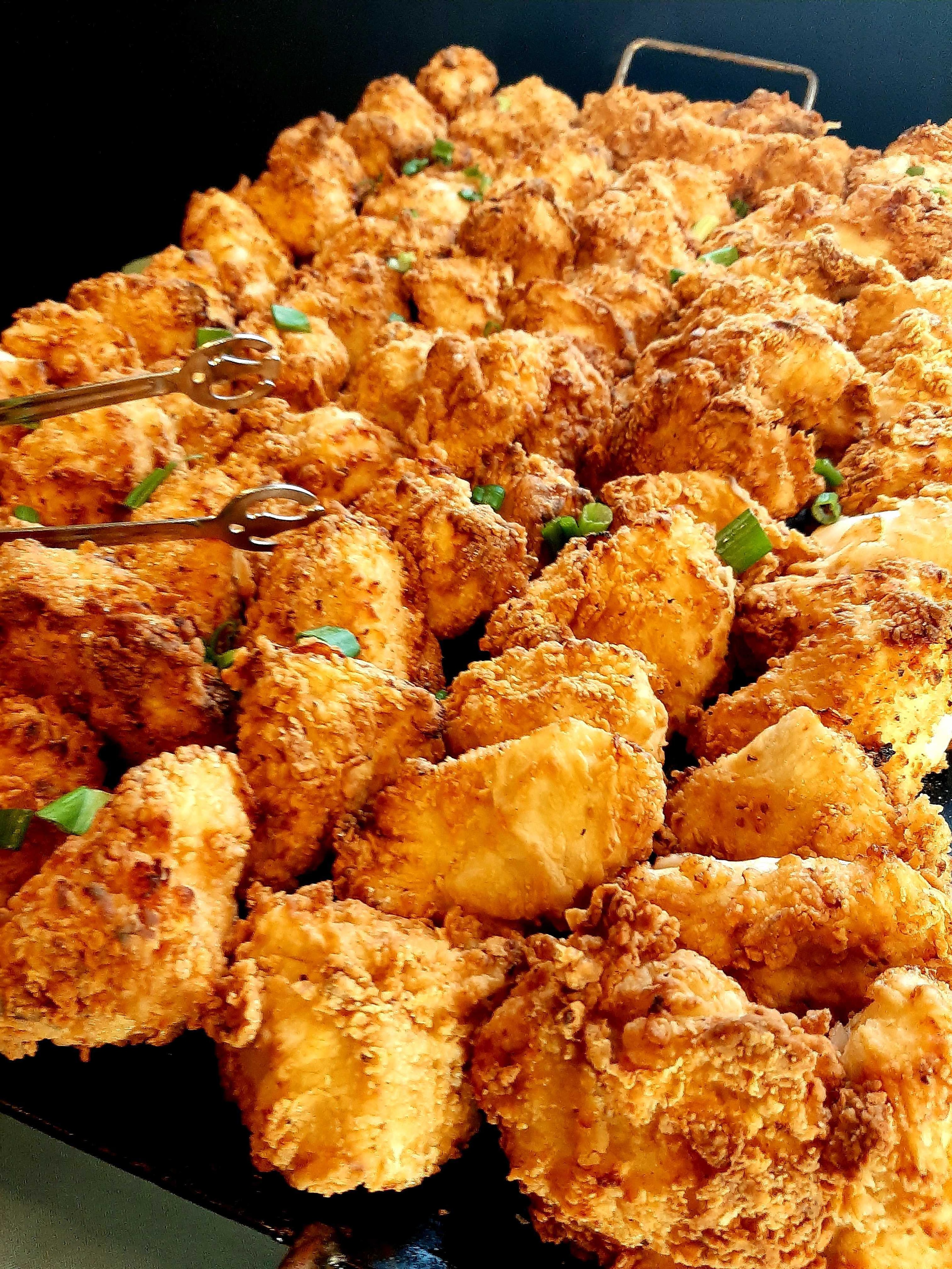 Cast-iron tray of crispy fried chicken bites with tongs and chive garnish — Atlanta film set catering