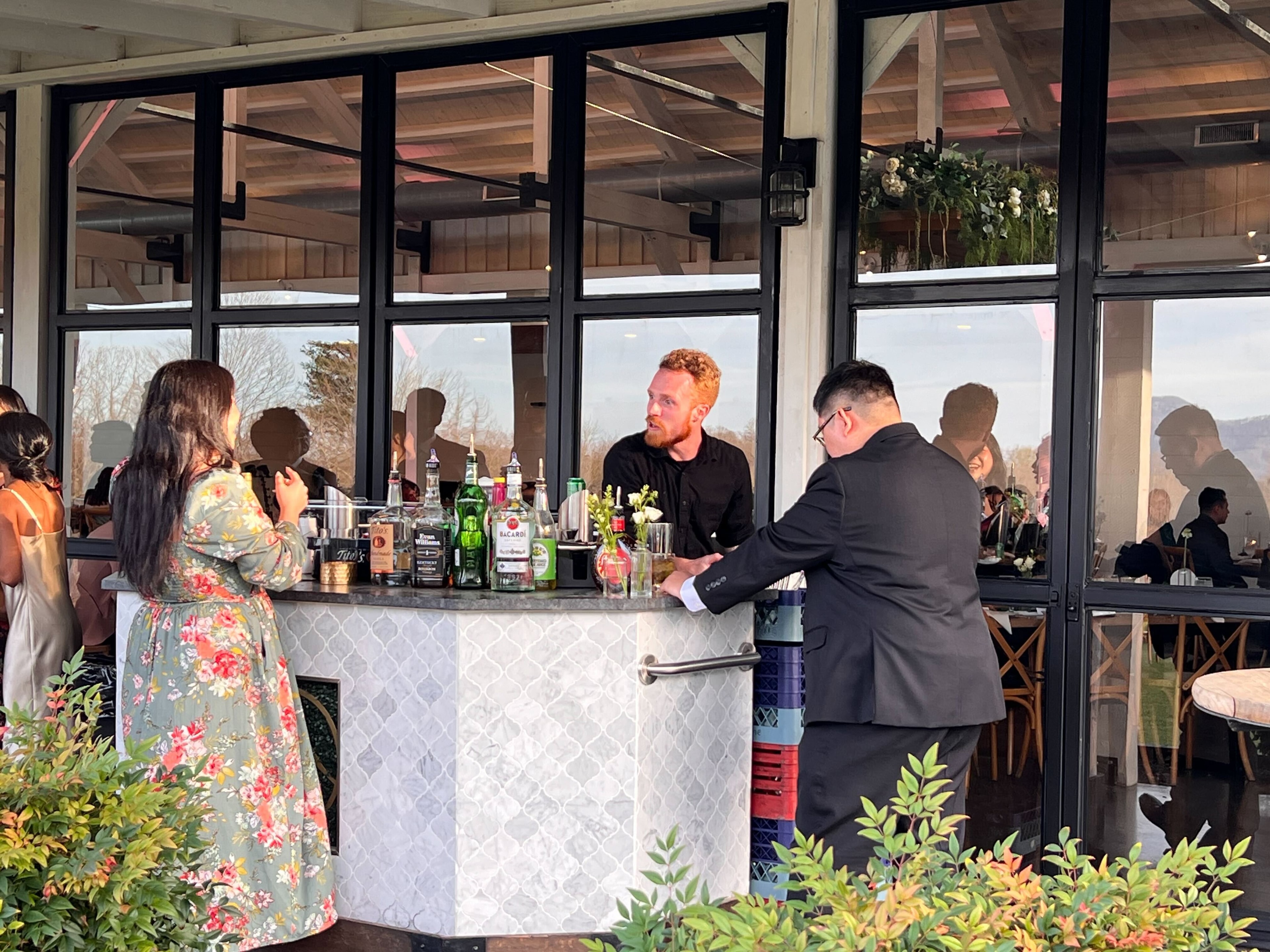 Atlanta Craft Services bartender serving guests at a marble bar in a covered outdoor event venue with Tito's, Bacardi, and Evan Williams bottles