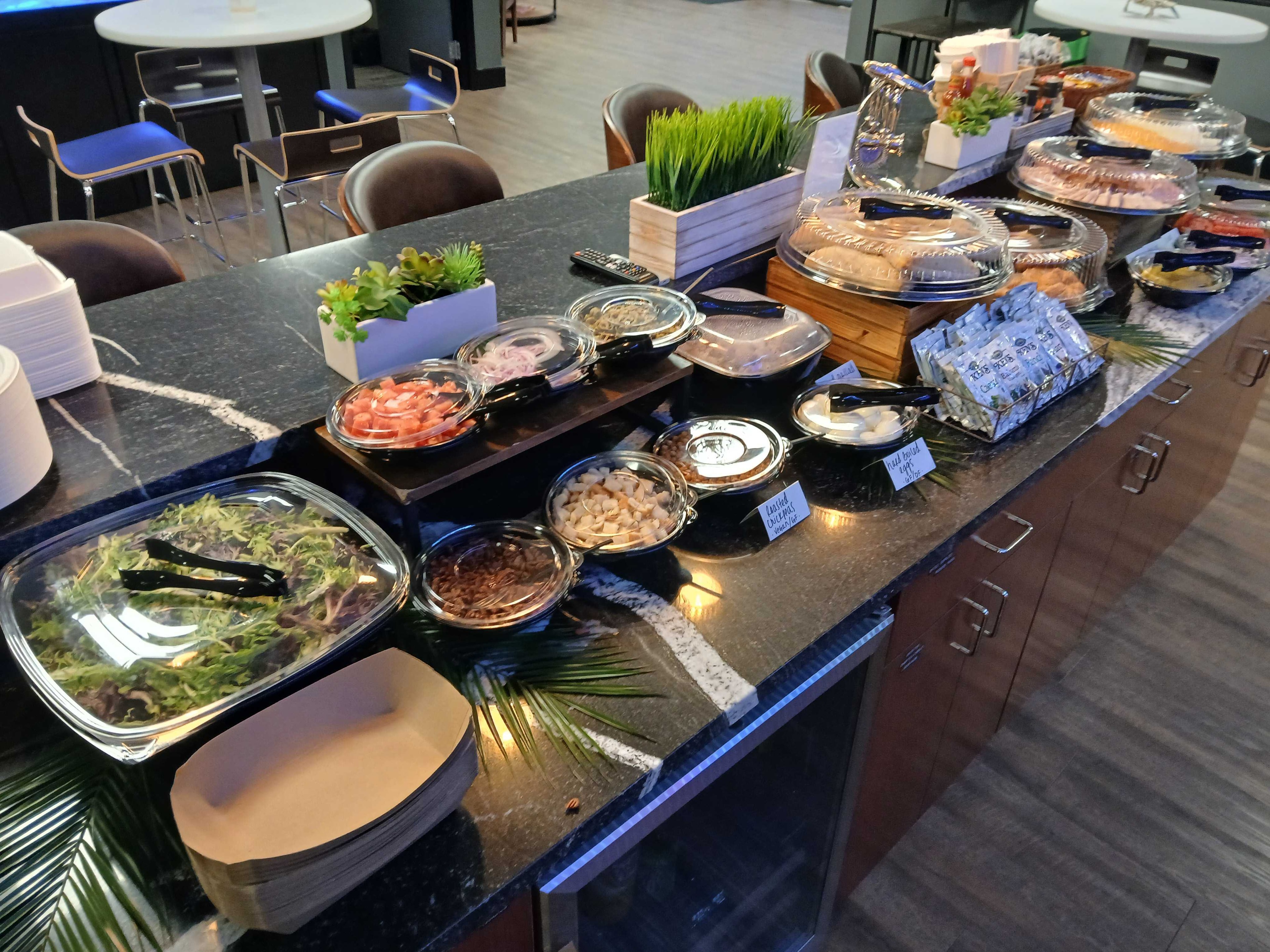 Corporate catering salad bar station on a dark granite counter with mixed greens, tomatoes, onions, chickpeas, deli meats, and Ken's dressing packets — Atlanta