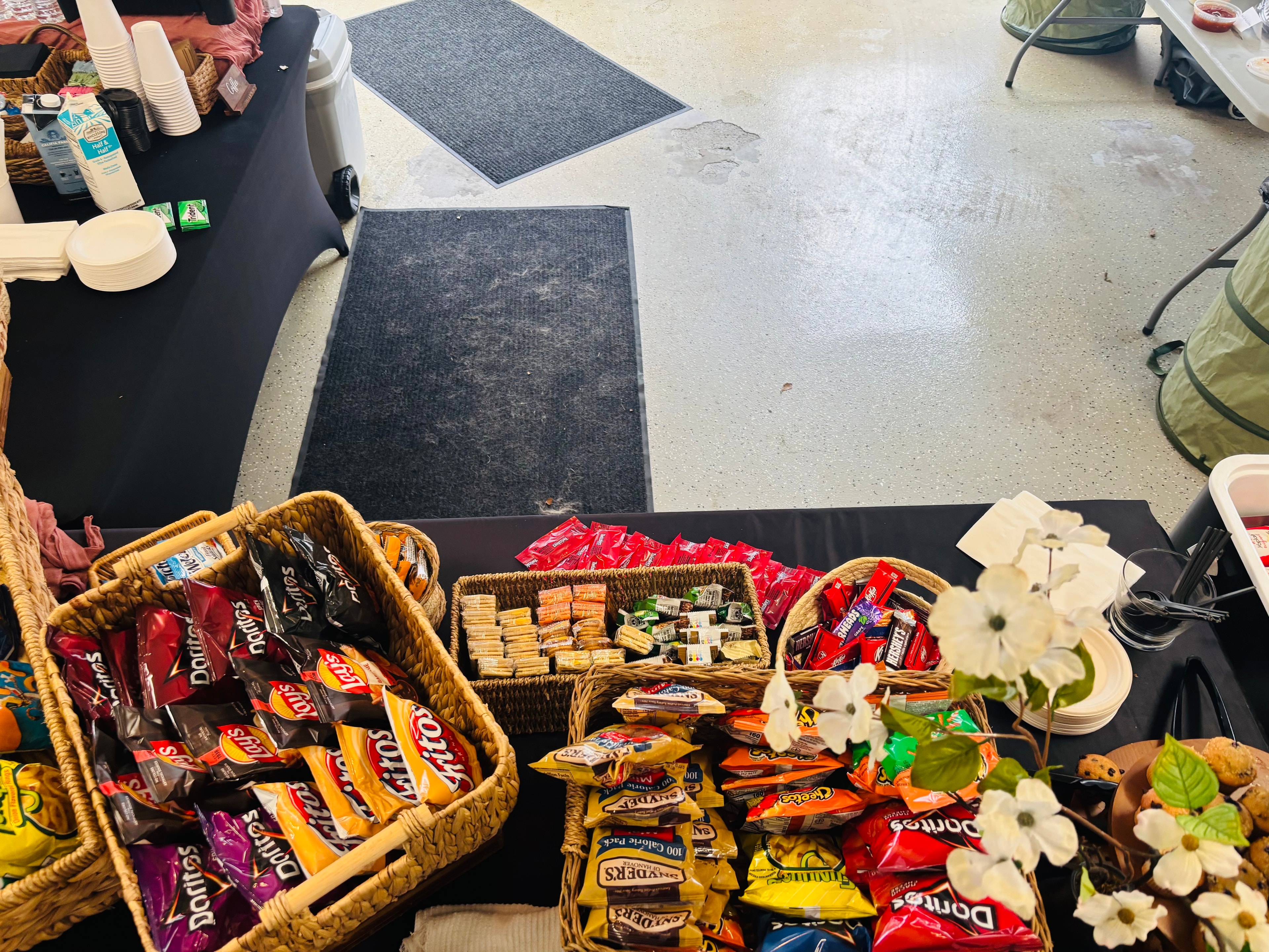 Atlanta craft service snack table with wicker baskets of Doritos, Fritos, Snyder's pretzels, granola bars, Hershey's, and Snickers with white flower arrangement