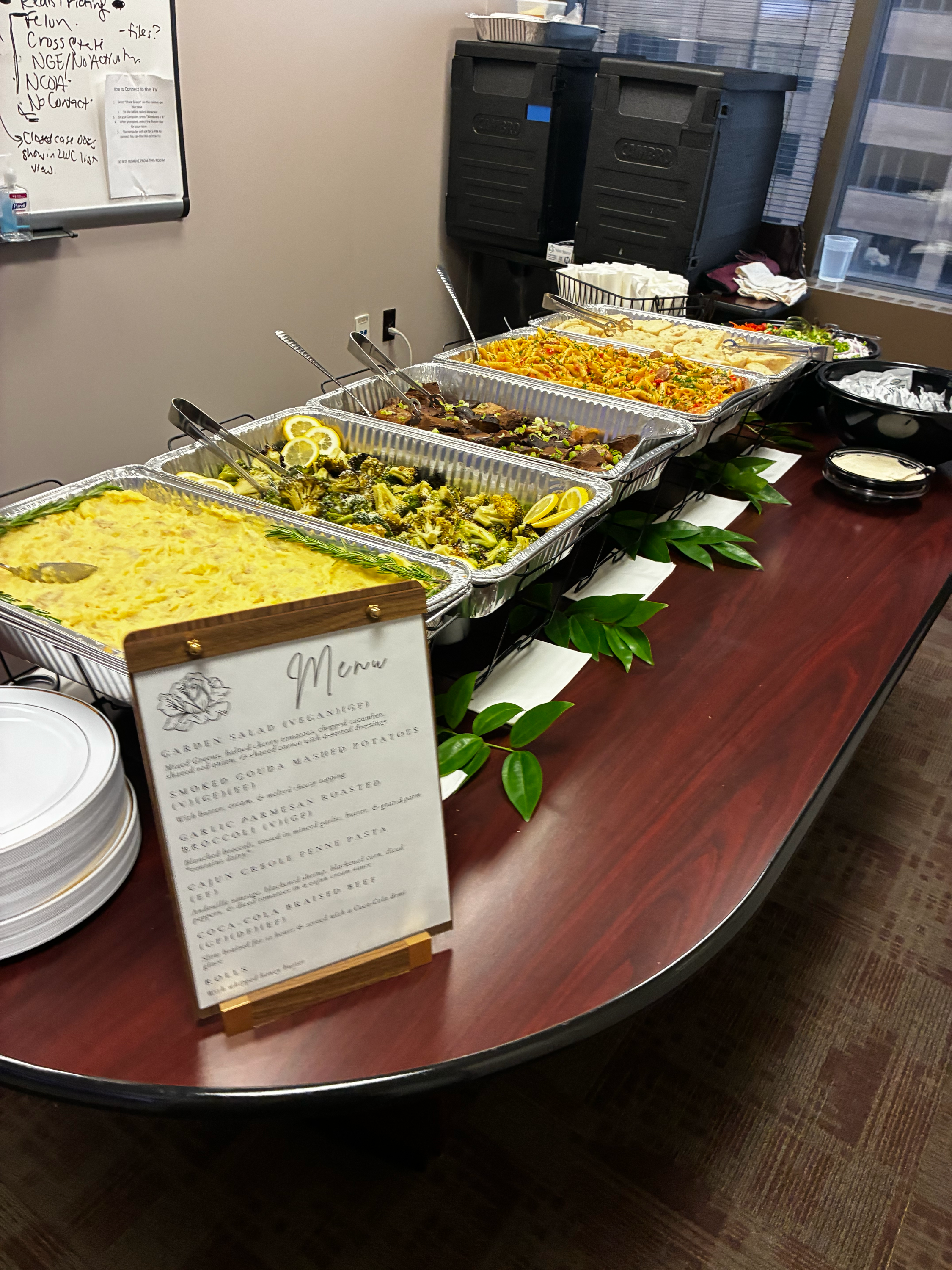 Atlanta office lunch catering spread with aluminum trays of smoked gouda mashed potatoes, garlic parmesan broccoli, Cajun Creole penne pasta, and Coca-Cola braised beef on a conference room table with a printed menu card