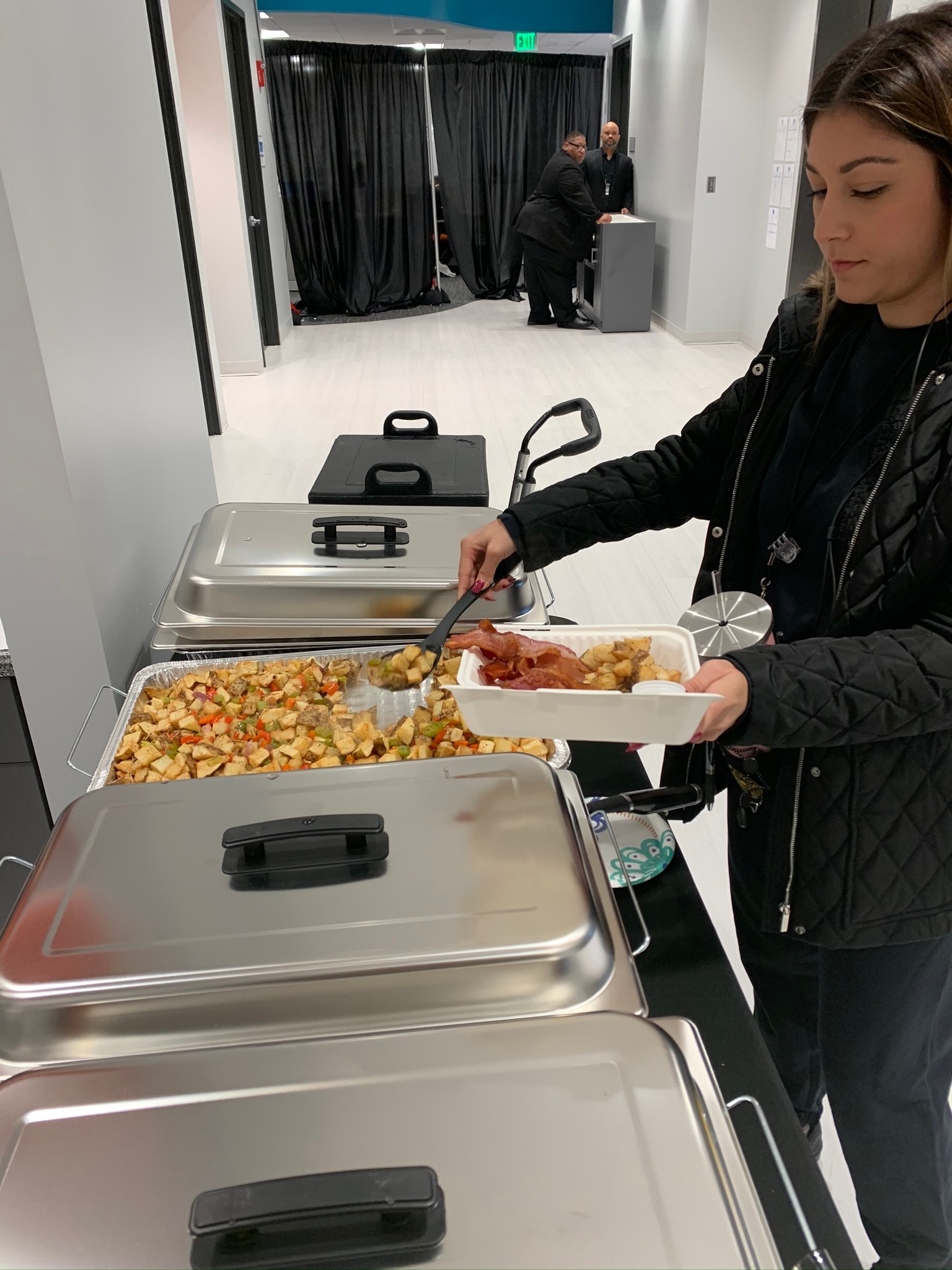 Crew member serving herself from chafing dishes of home fries and bacon at an indoor film production catering buffet — Atlanta