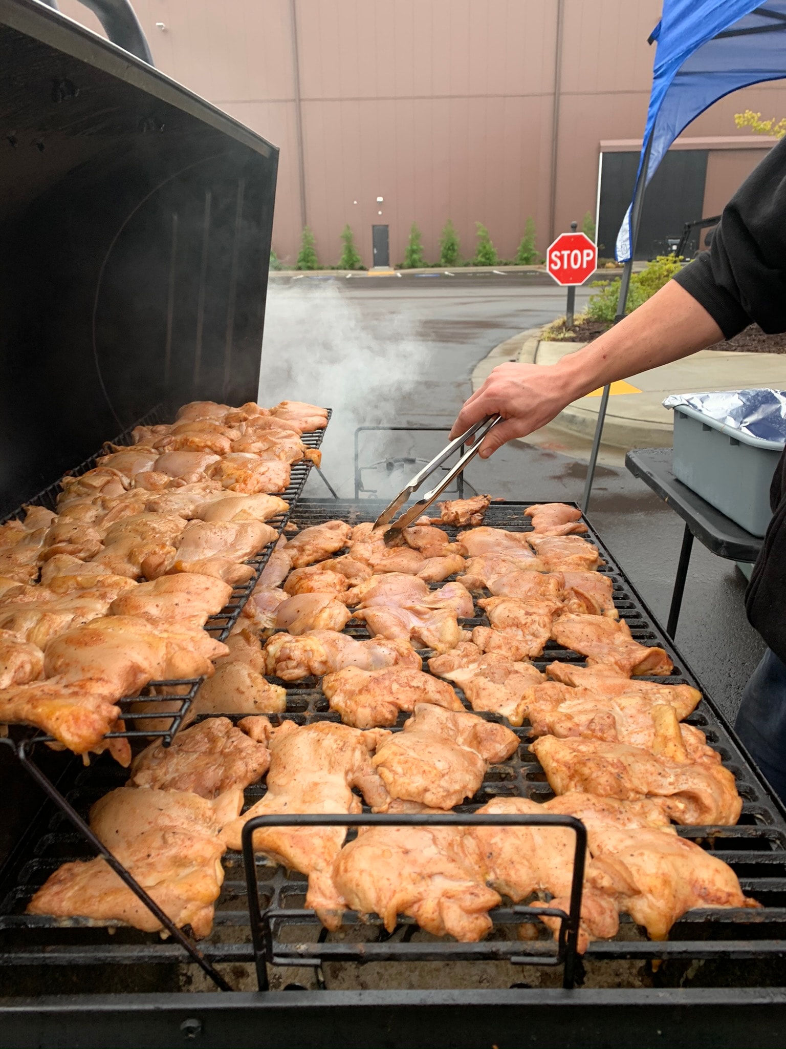 Large outdoor grill loaded with marinated chicken thighs being tended with tongs — Atlanta film production catering