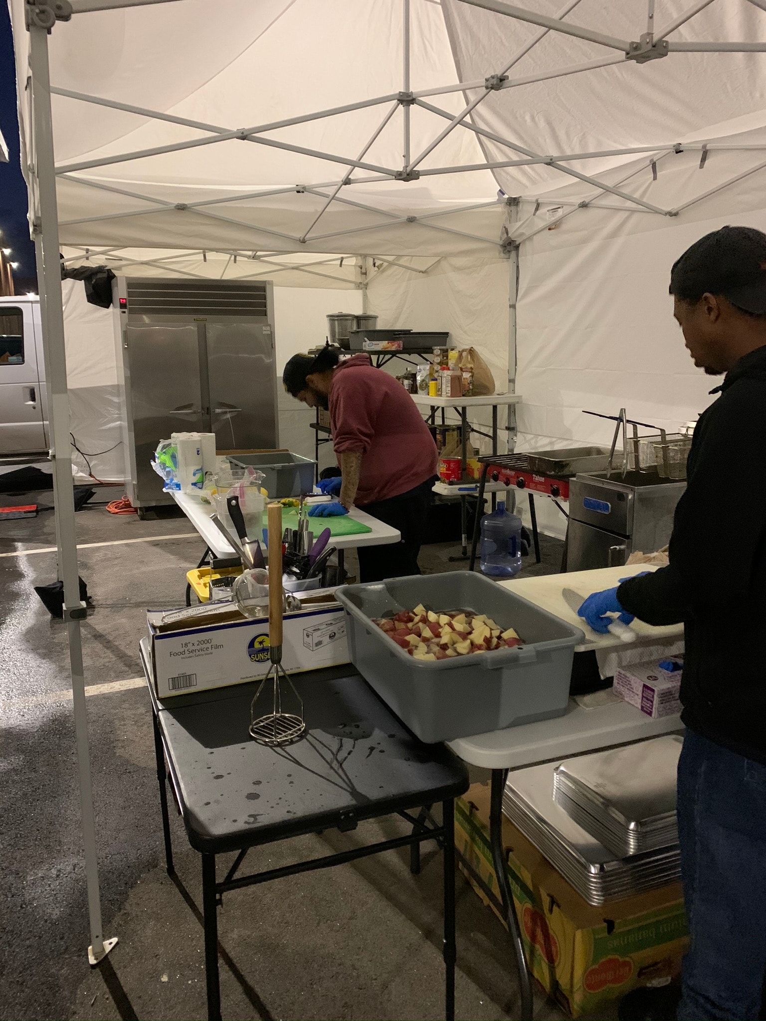 Two chefs prepping food under a tent at night with commercial kitchen equipment including a large refrigerator — Atlanta film production catering