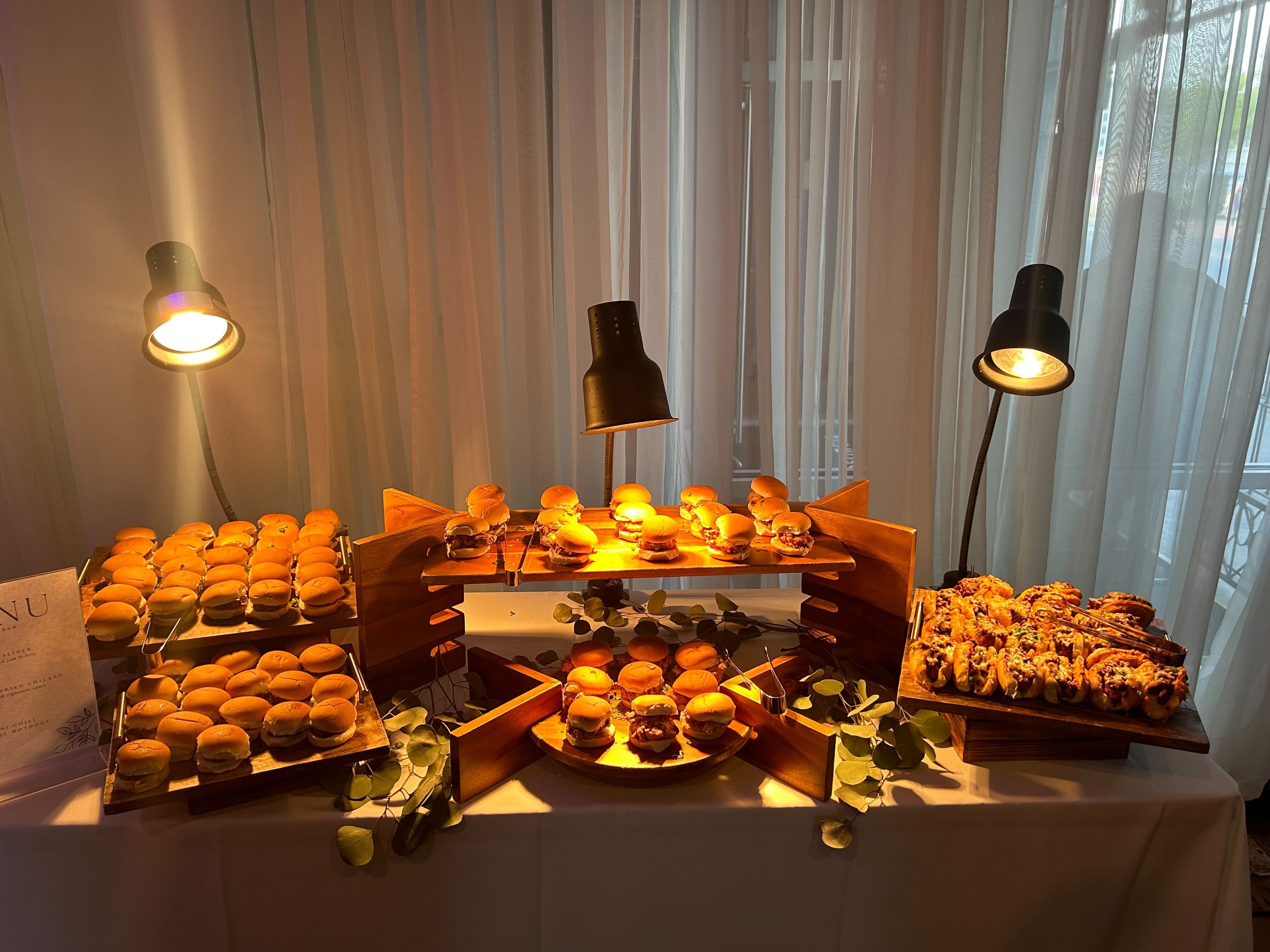 Elegantly lit slider and pastry display on tiered wooden stands with warm heat lamp lighting — Atlanta production catering